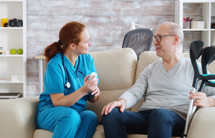 In retirement home nurse is talking with elderly man about drugs dosage. Caregiver and social worker