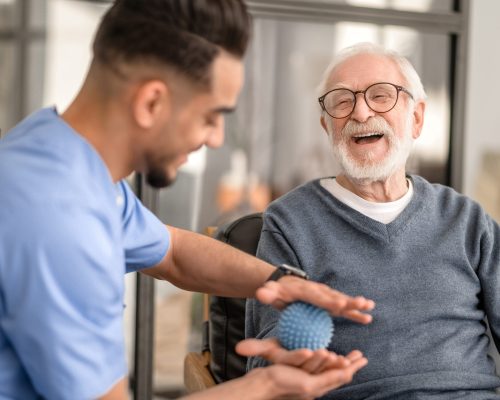 Joyous aged man undergoing a session of physical therapy conducted by an experienced rehabilitation doctor